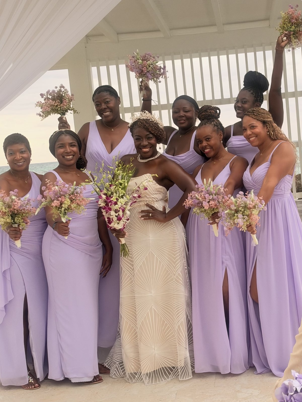 Christal in her wedding gown with seven smiling bridesmaids in lavender, holding bouquets in the air
