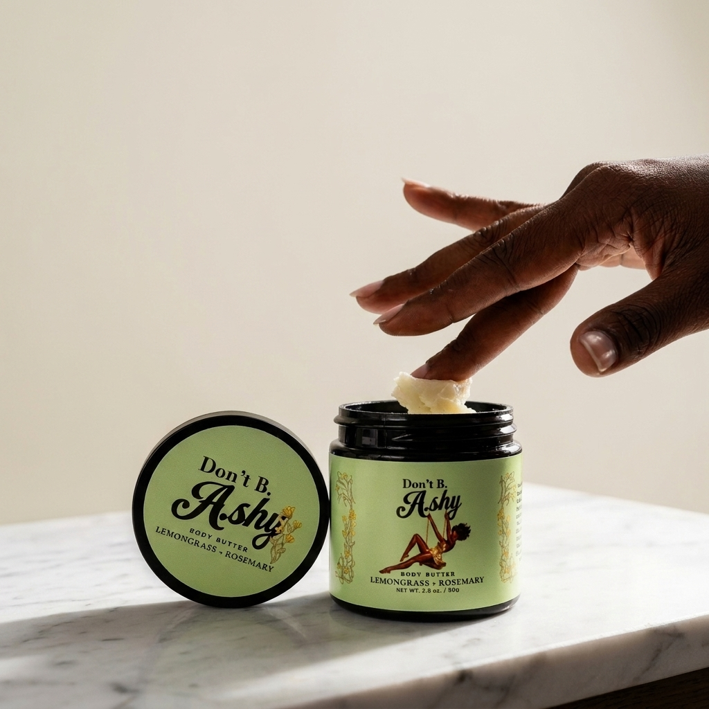 A hand dipping two fingers into an open jar of Don't B. Ashy Lemongrass + Rosemary body butter on a marble counter